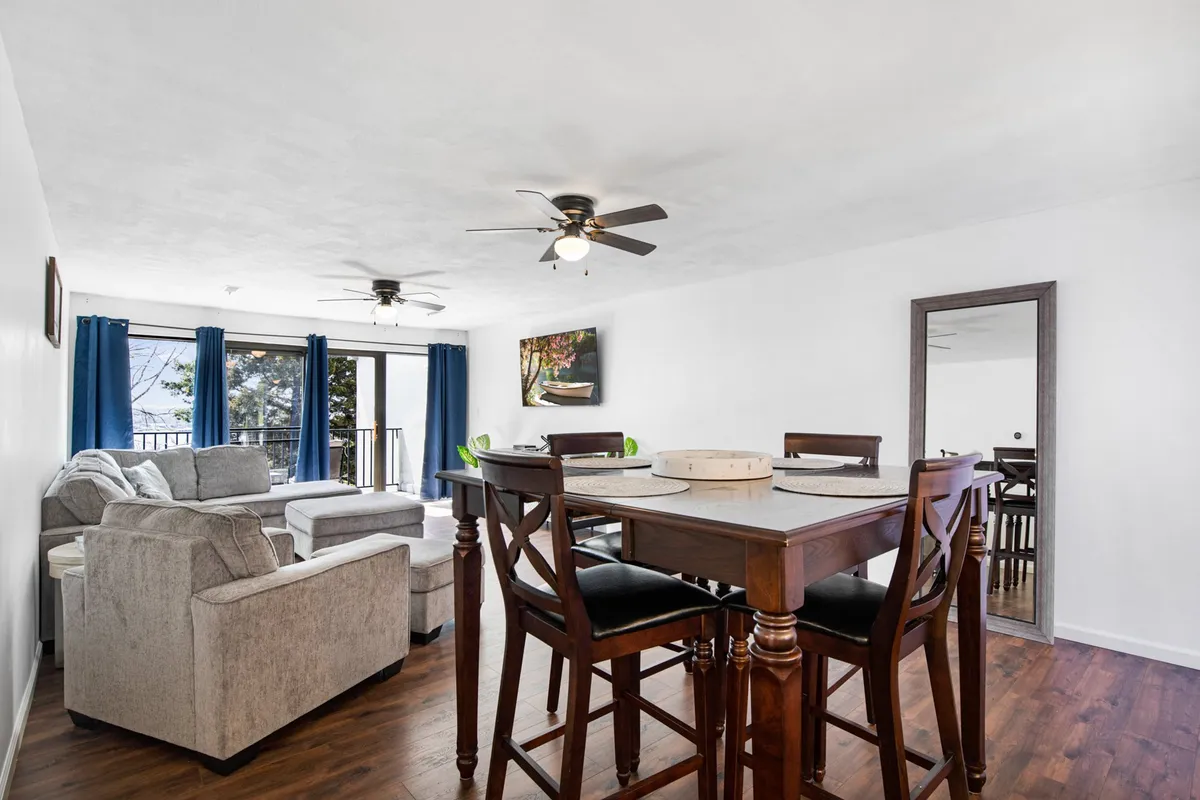 Here, a dining table anchors a spacious interior, adjacent to a soft sofa and highlighted by large windows dressed with curtains. An art piece decorates the wall, reinforcing the space’s modern aesthetic and its suitability for both relaxing and socializing.