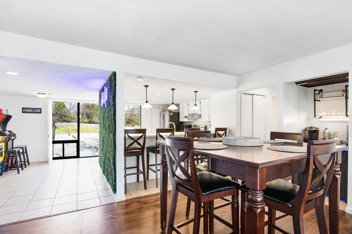 A bright, open dining area with a dining table set against a green accent wall, with arcade games and a view into the kitchen area. The space is ideal for family meals, game nights, and casual brunches.