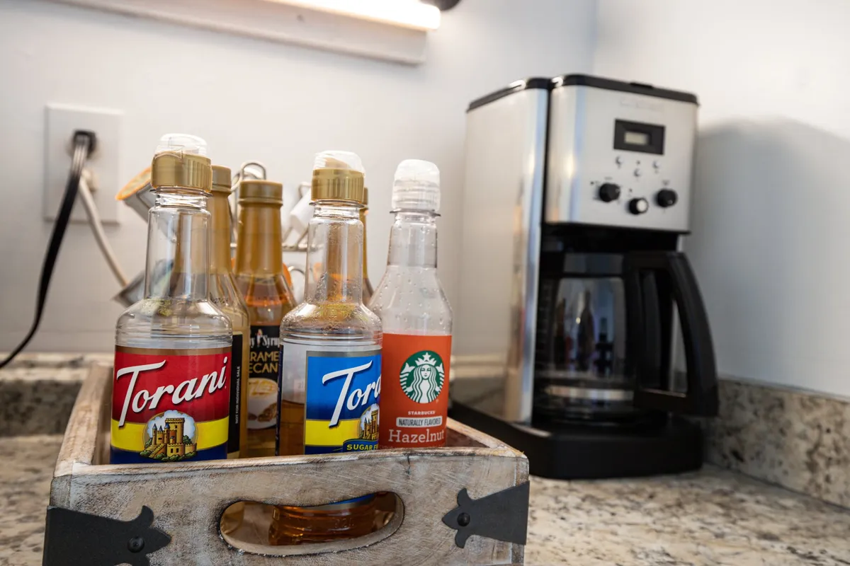A cozy coffee bar setup featuring a modern coffee maker and an array of flavored syrups, inviting guests to craft their own personalized beverages. The intimate setting encourages morning rituals and social connection.