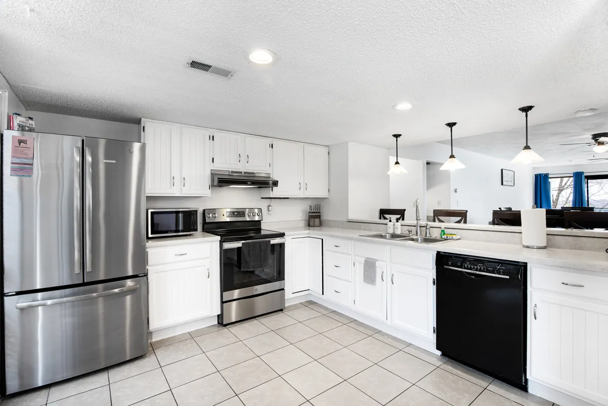 A modern kitchen featuring stainless steel appliances, white cabinetry, a spacious kitchen island with seating, and elegant pendant lighting. The area is well-lit and designed for both cooking and social gatherings.