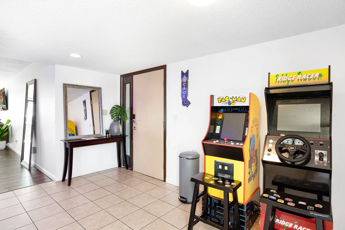 A welcoming scene with multiple arcade machines, a mirror, an entrance door hinting at easy comings and goings, and a touch of greenery. The area is set up for social gaming and shared laughter, echoing the lively energy of nearby attractions.