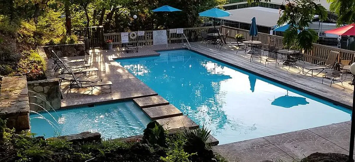 This exterior image features a sparkling swimming pool surrounded by lounge chairs, a hot tub, umbrellas, and lush greenery. The tranquil setting is ideal for family relaxation after a day of adventure, with plenty of space for swimming, sunbathing, and socializing.