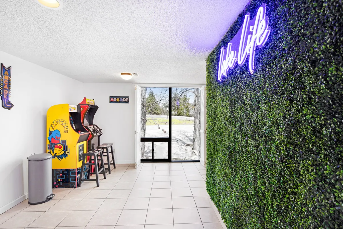 This image features a nostalgic arcade machine set against a playful green wall with a neon sign, evoking a fun, retro vibe. The setup hints at a dedicated space for gaming and socializing, with elements like snacks and drinks visible, showing a lively, interactive environment.