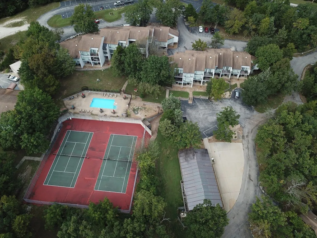 An expansive exterior view showing tennis courts, a swimming pool, lush greenery, and nearby buildings, capturing communal amenities and the broader outdoor setting. The openness and activity potential reflect the spirit of exploration and active experiences, ideal for guests and pets who enjoy the outdoors.