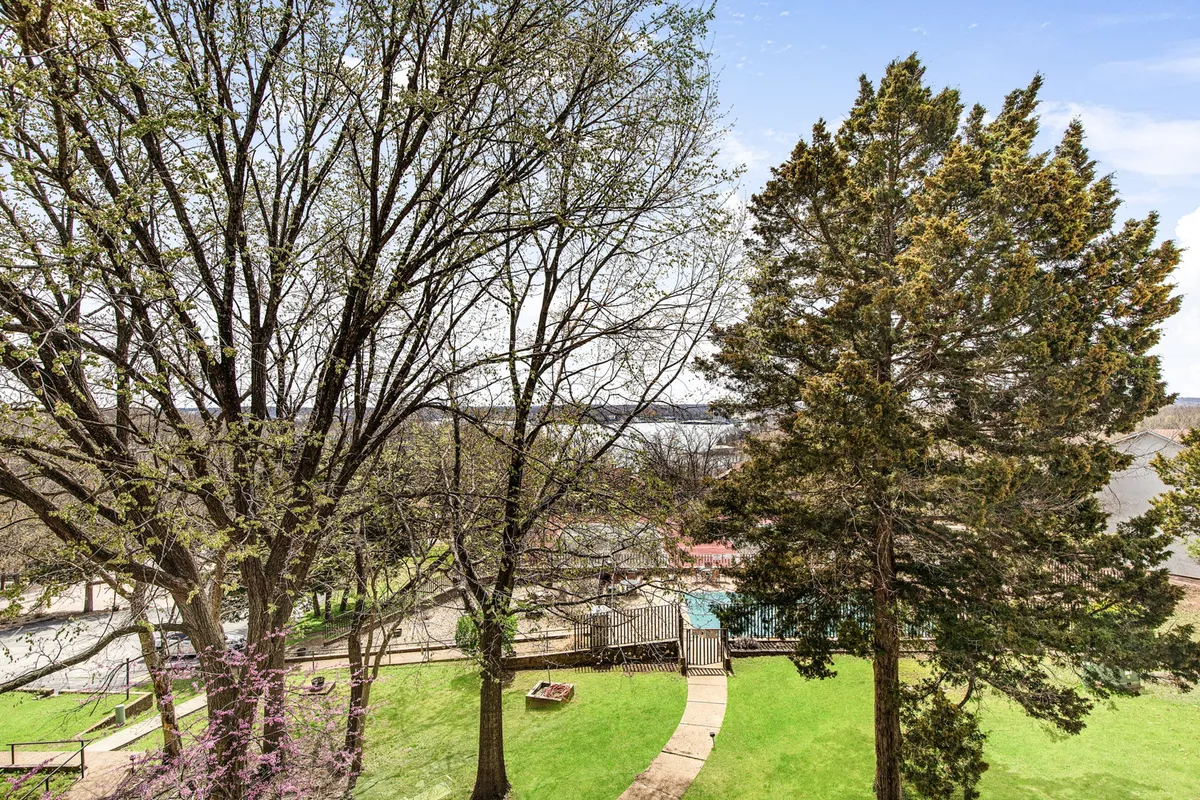 This wide-angle exterior shot captures a lush green lawn bordered by tall trees and a swimming pool area with a winding pathway. The space is perfect for outdoor play, nature walks, and summer picnics.